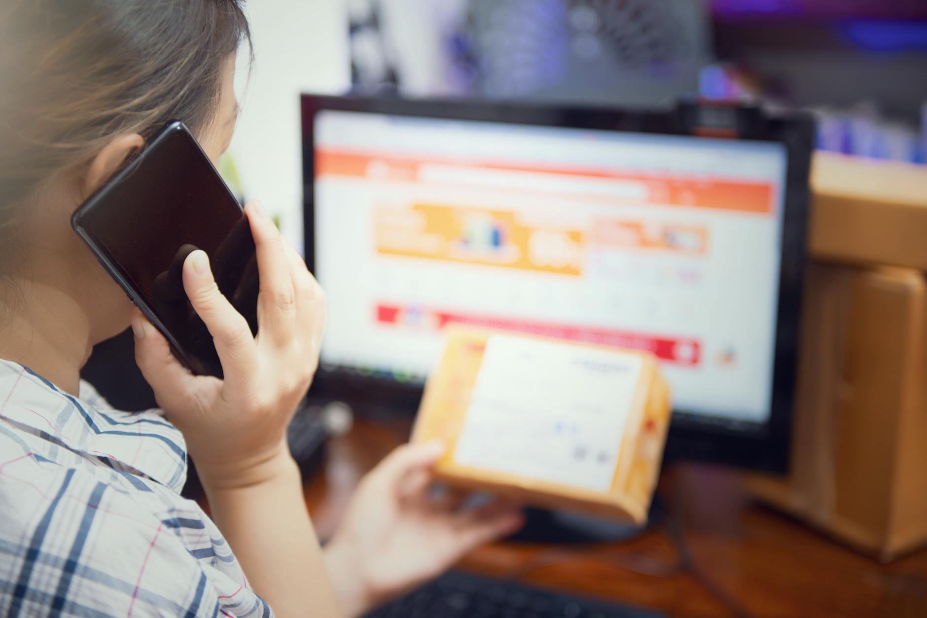 Kobieta w domu sprawdza paczkę z zakupami online, rozmawiając przez telefon