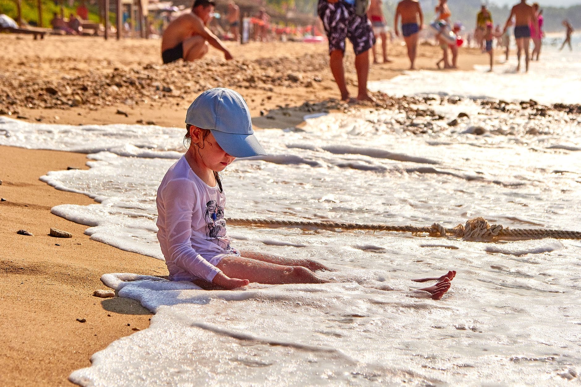 Małe dziecko bawi się w morskich falach na zatłoczonej plaży