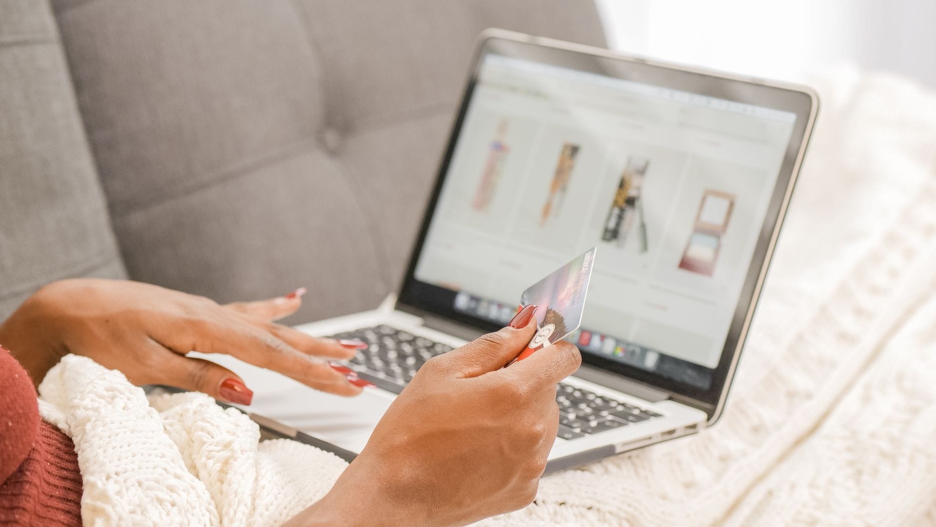 Kobieta na kanapie robi zakupy online na laptopie, trzyma kartę kredytową