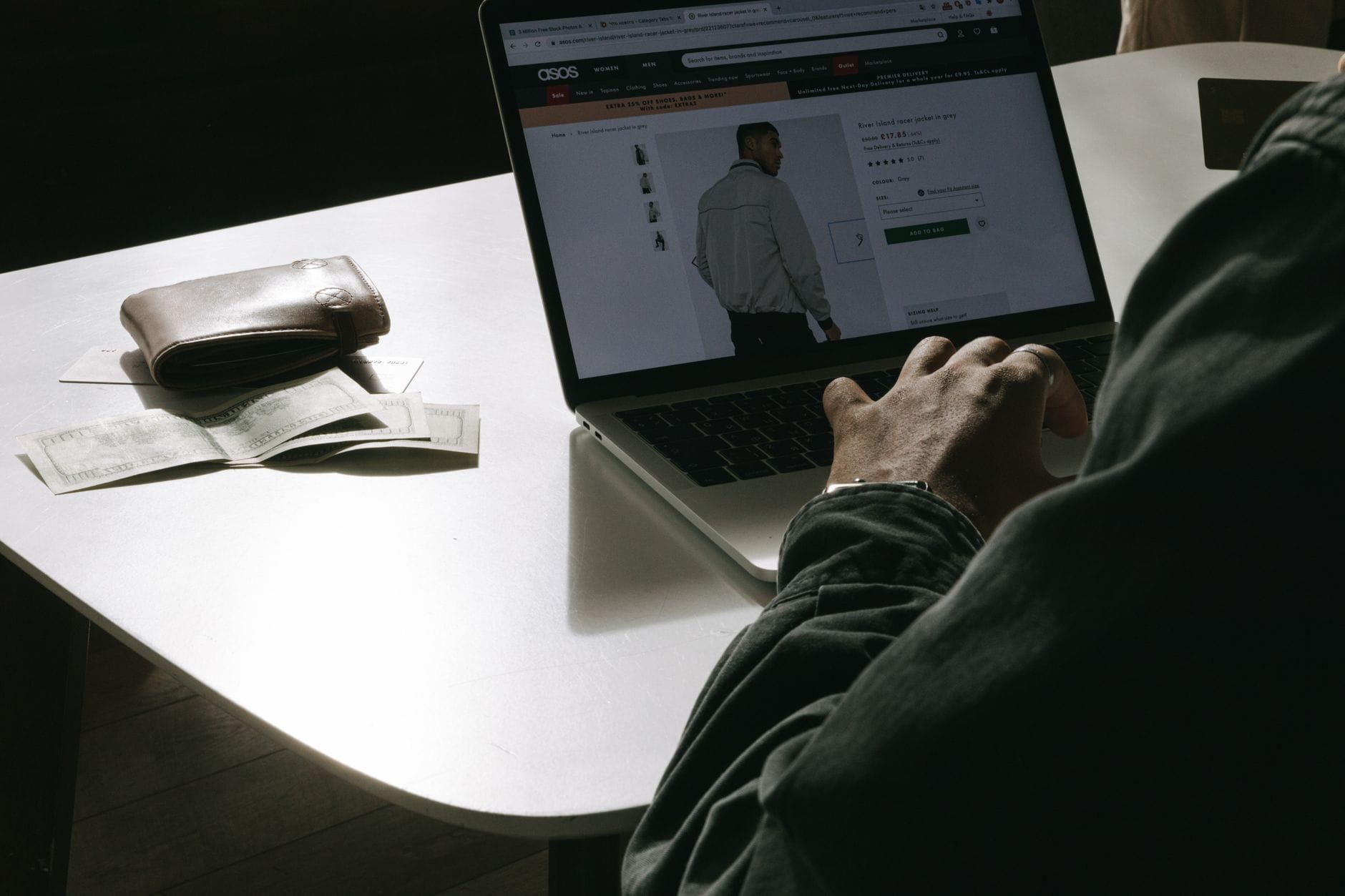 Mężczyzna kupuje ubrania online na laptopie, portfel na stole